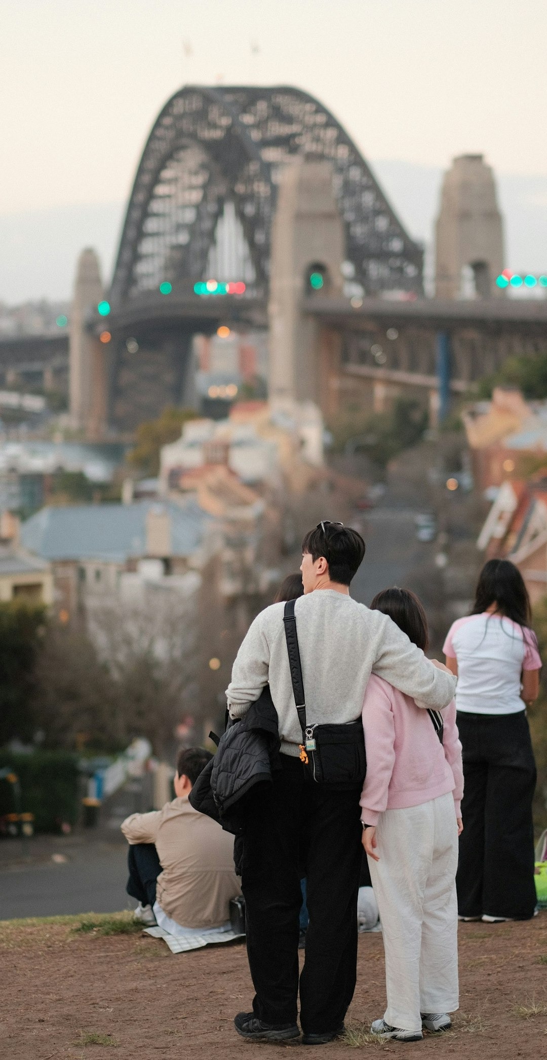 Een man en vrouw met aziatisch uiterlijk die elkaar vasthouden. Op de achtergrond zie je andere mensen en de skyline van een stad, waaronder een grote brug